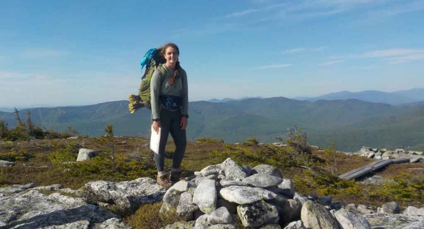 A person stands on an overlook with green mountains in the background. 